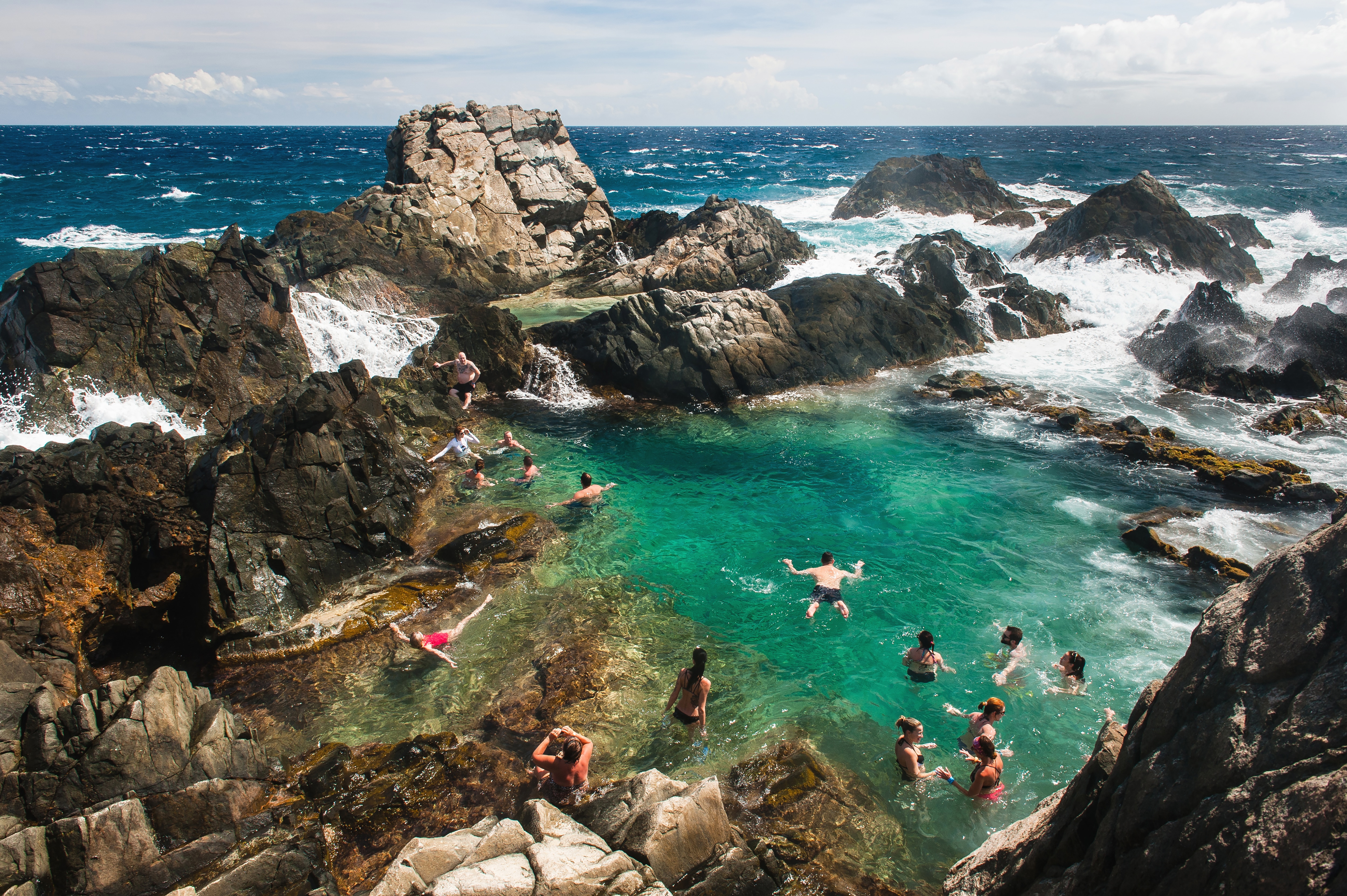 People swim in crystal-clear waters surrounded by rugged rocks at Arikok National Park in Aruba 