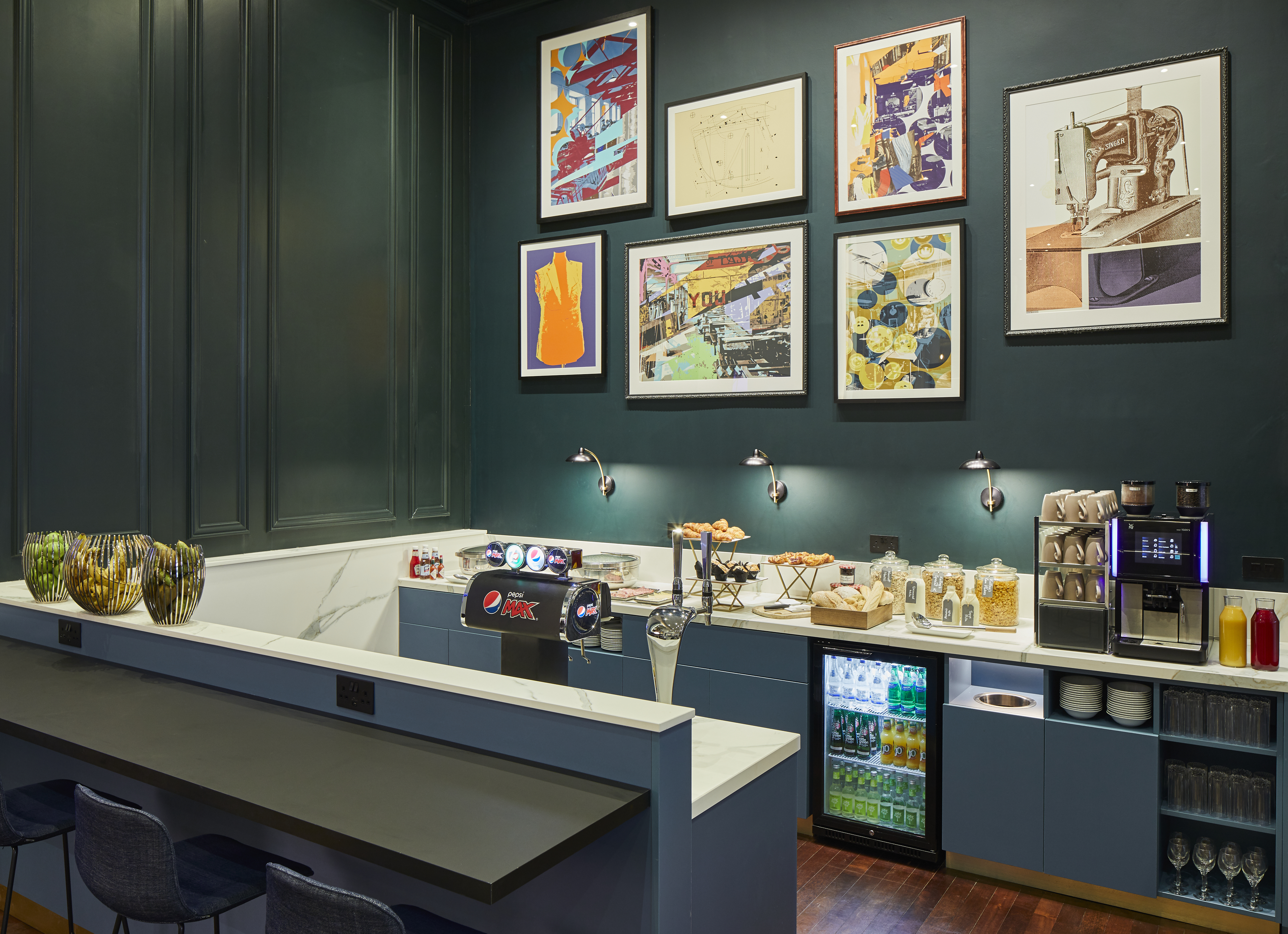 Counter displaying snacks and beverages in front of dark green wall with framed art pieces