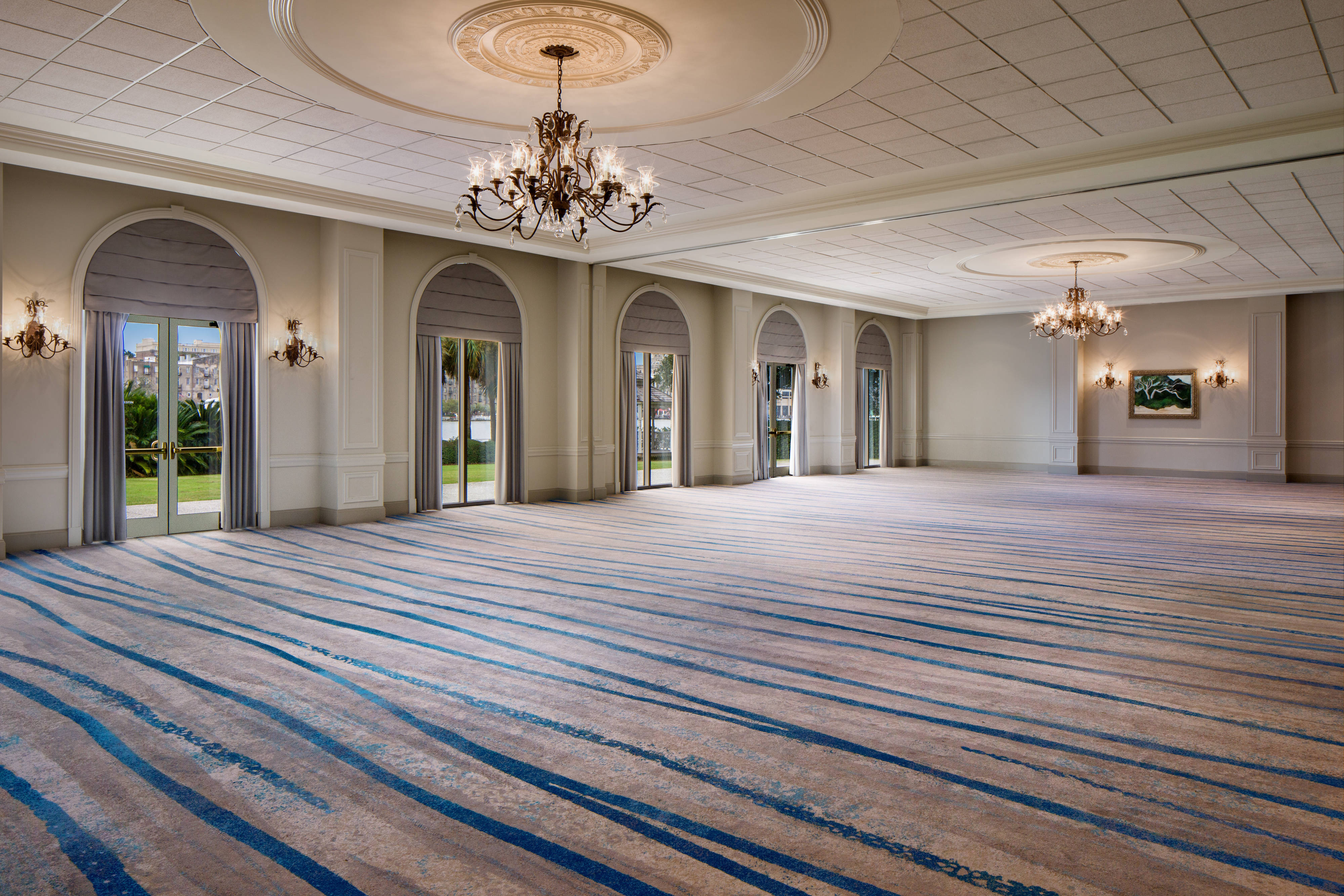 Carpeted ballroom with chandeliers and tall windows and glass doors offering a view