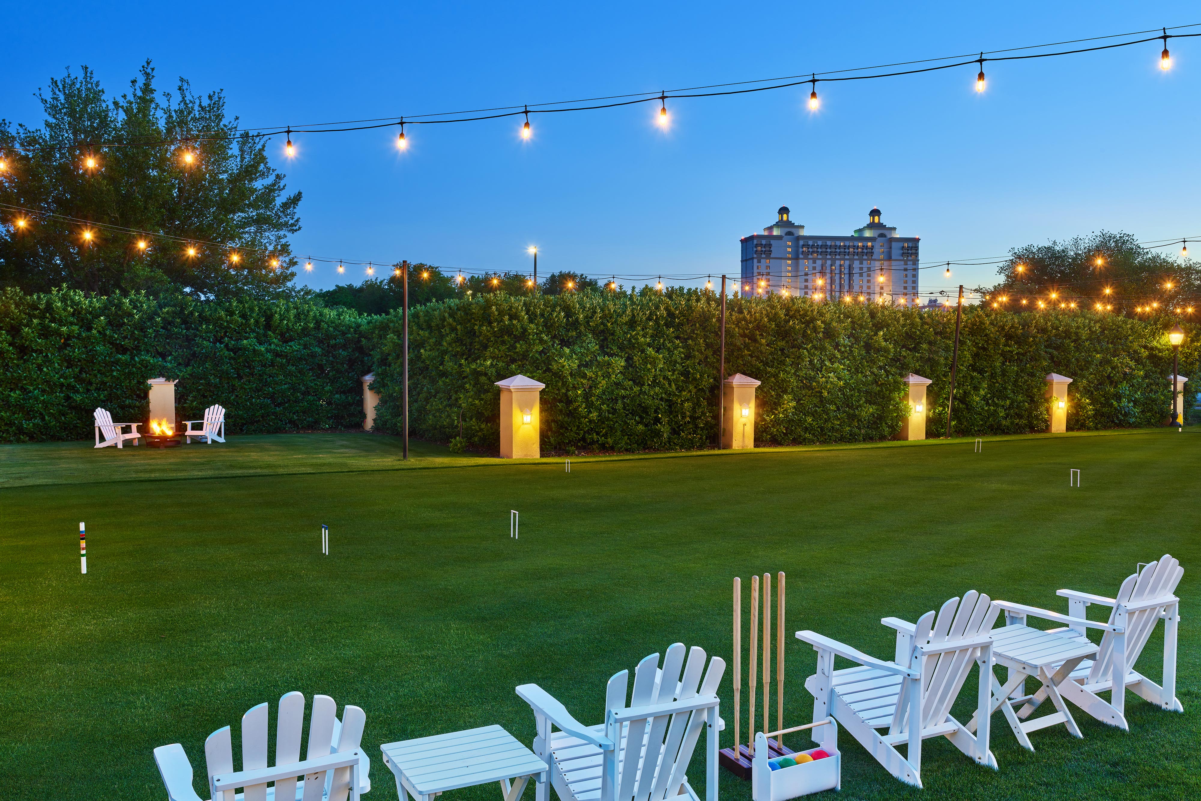 Manicured course with a croquet set and lawn chairs, lit with overhead string lights