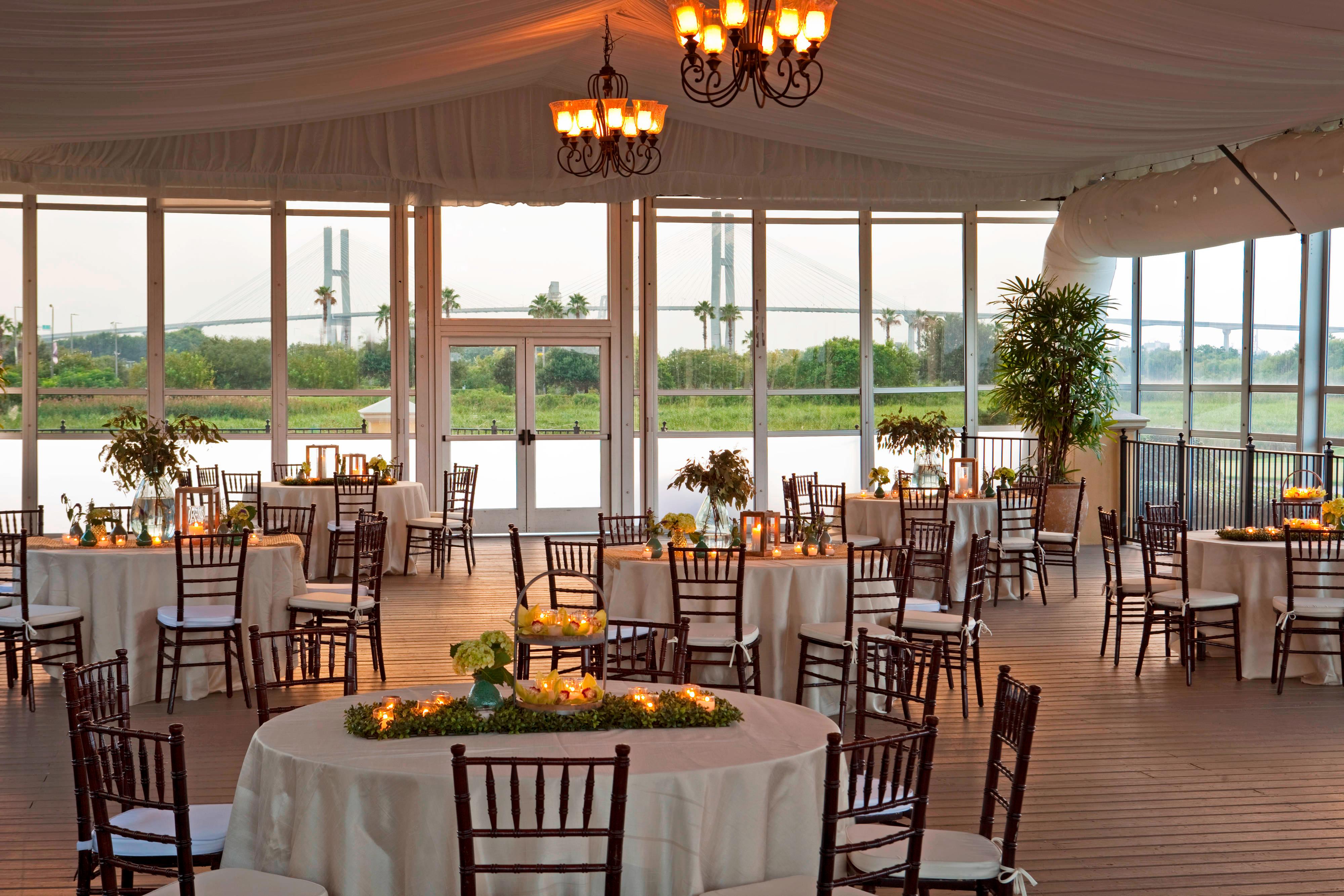 Glass-walled Club Pavilion set for wedding reception with round tables, flowers and candles