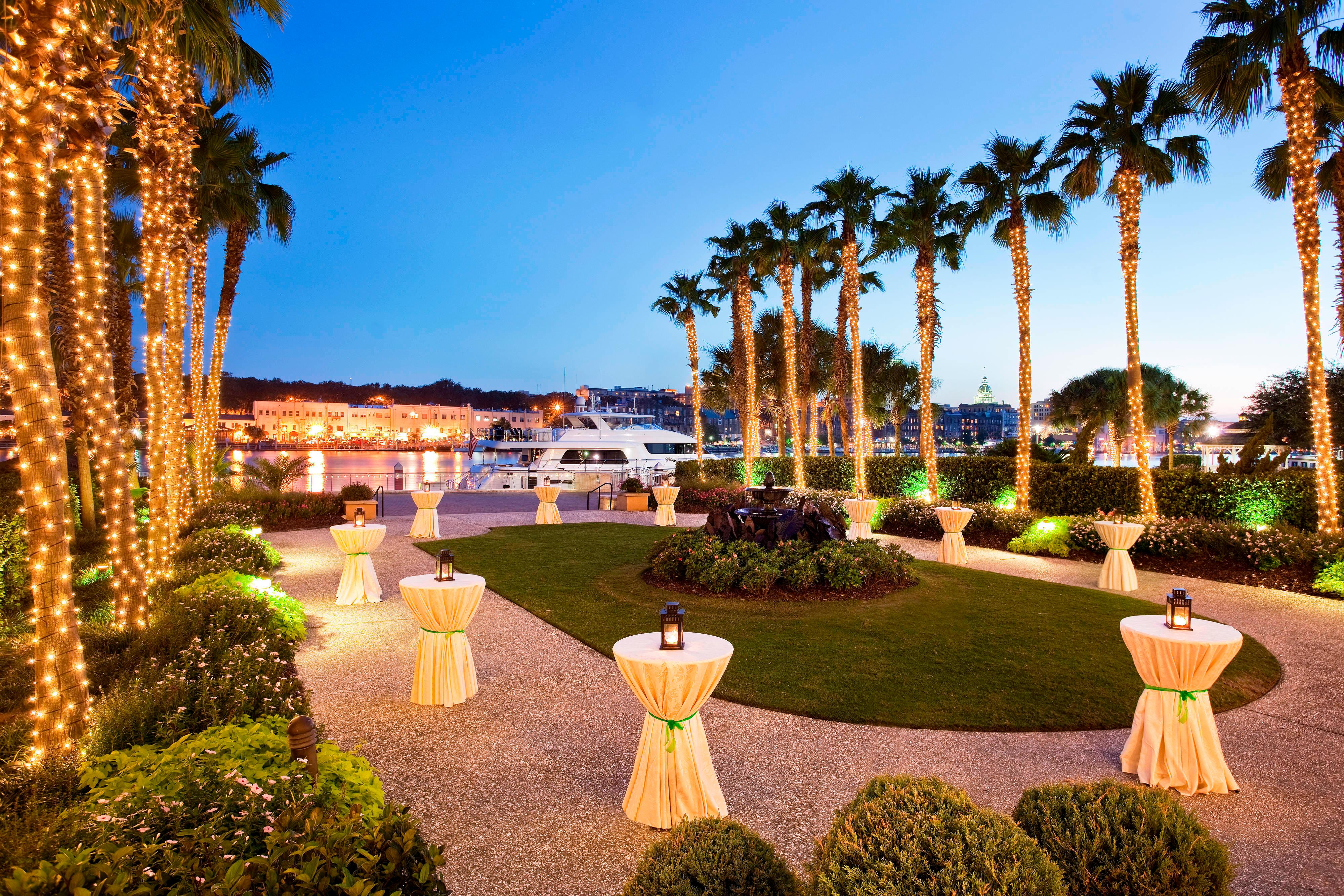 Landscaped oval lawn on the waterfront lined with palm trees wrapped in white string lights