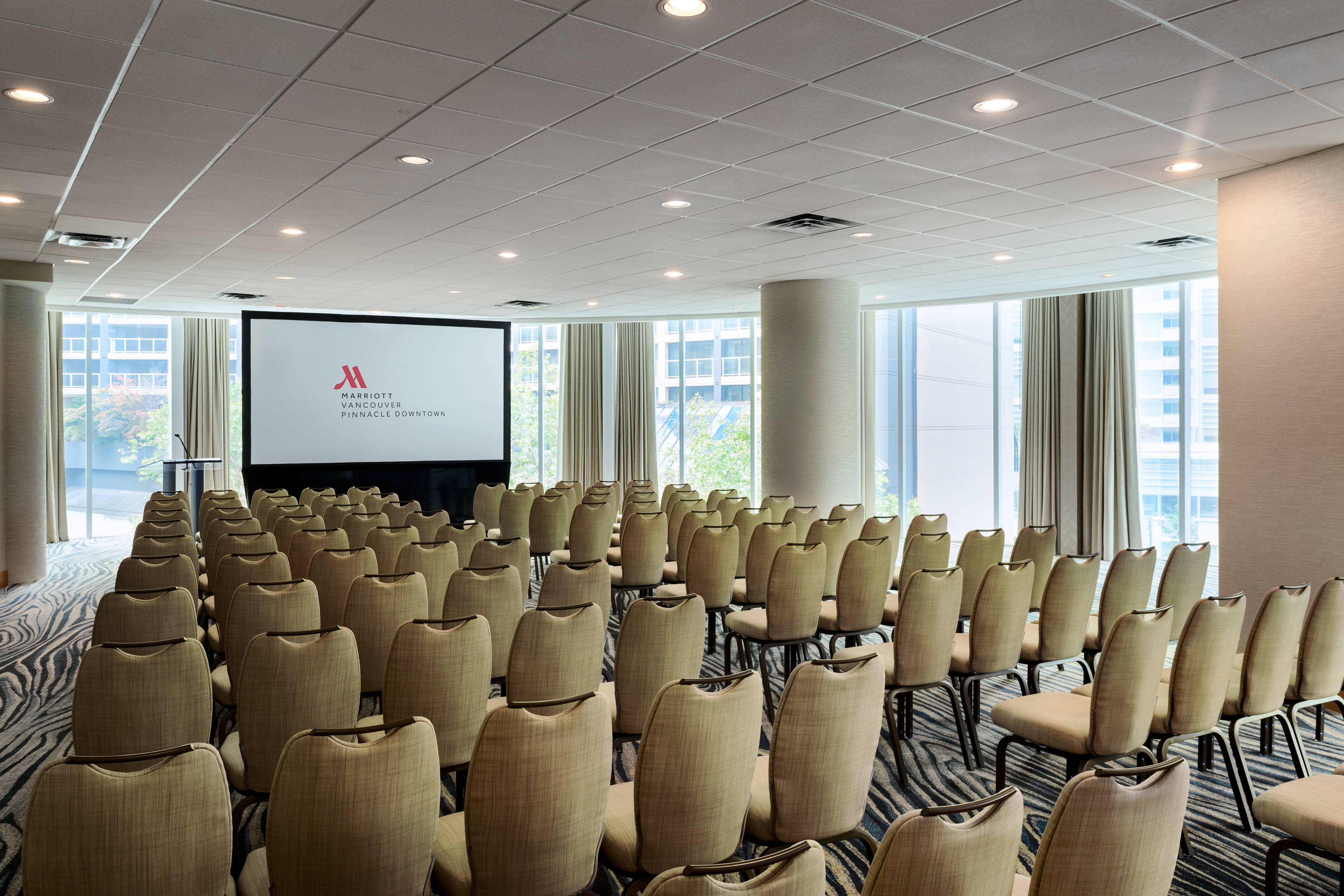 Chairs arranged in rows before a projector screen in a sunny, large meeting room.