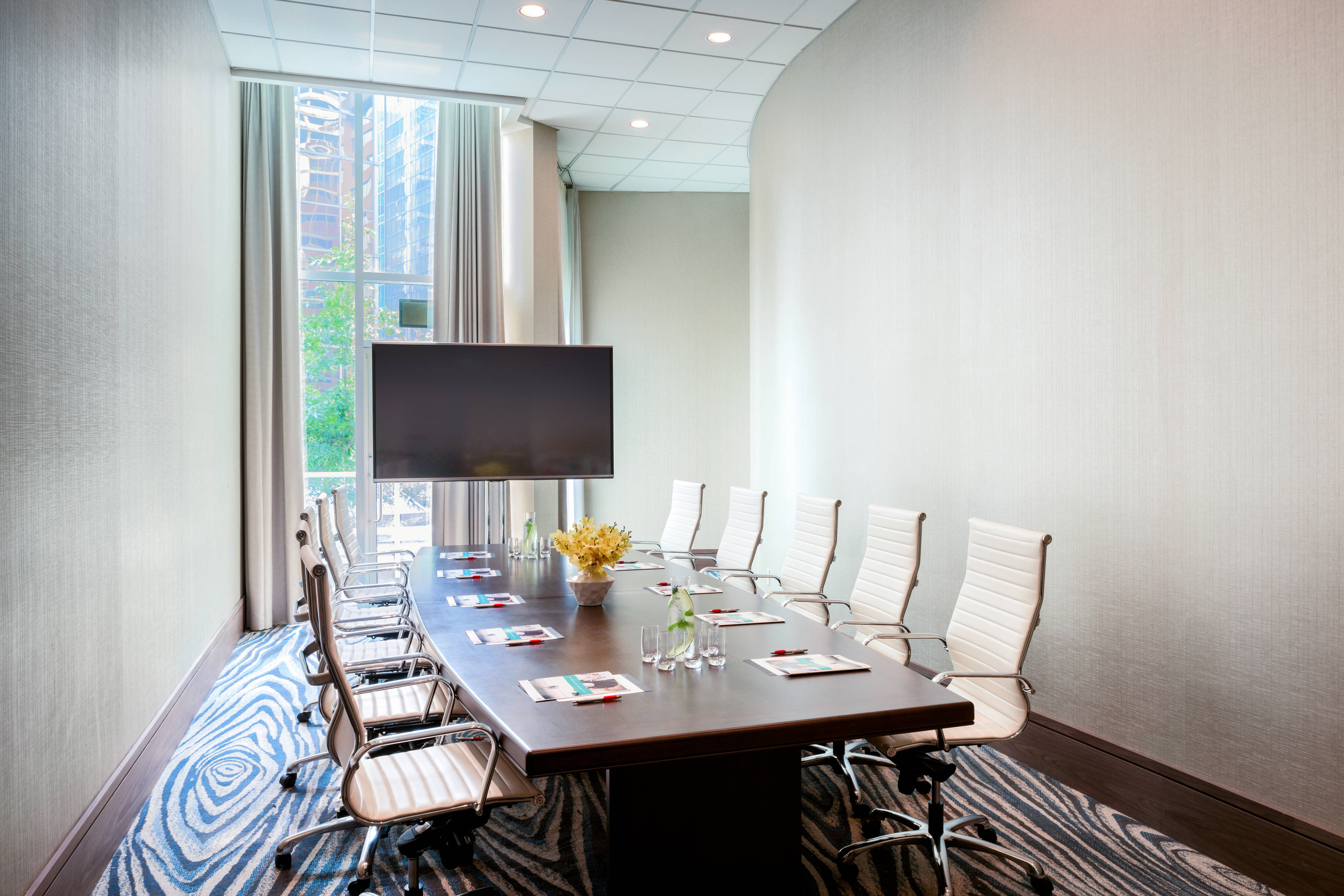 A conference table with a projector screen in a room with tall windows.