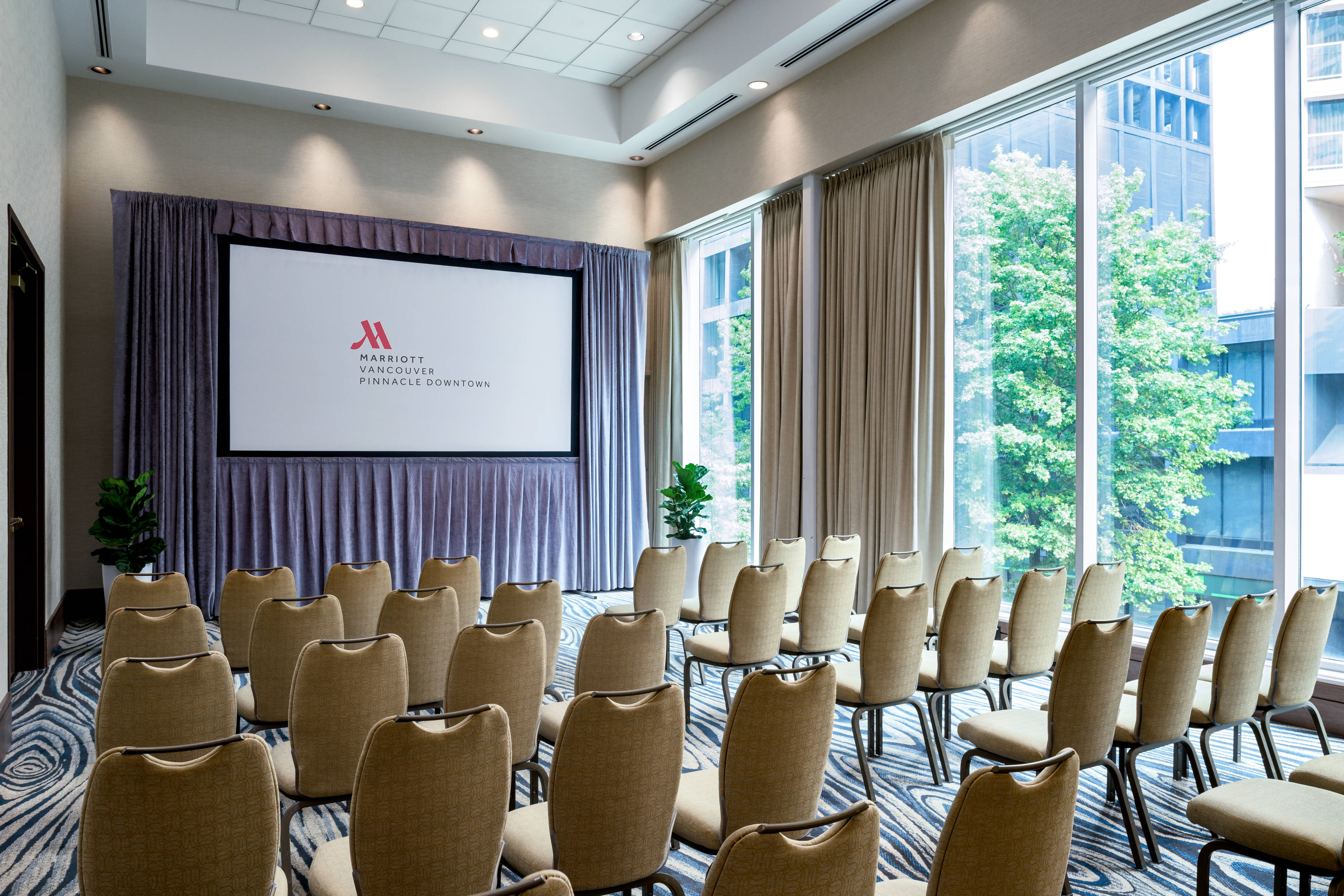 Chairs arranged in rows before a projector screen next to large windows.
