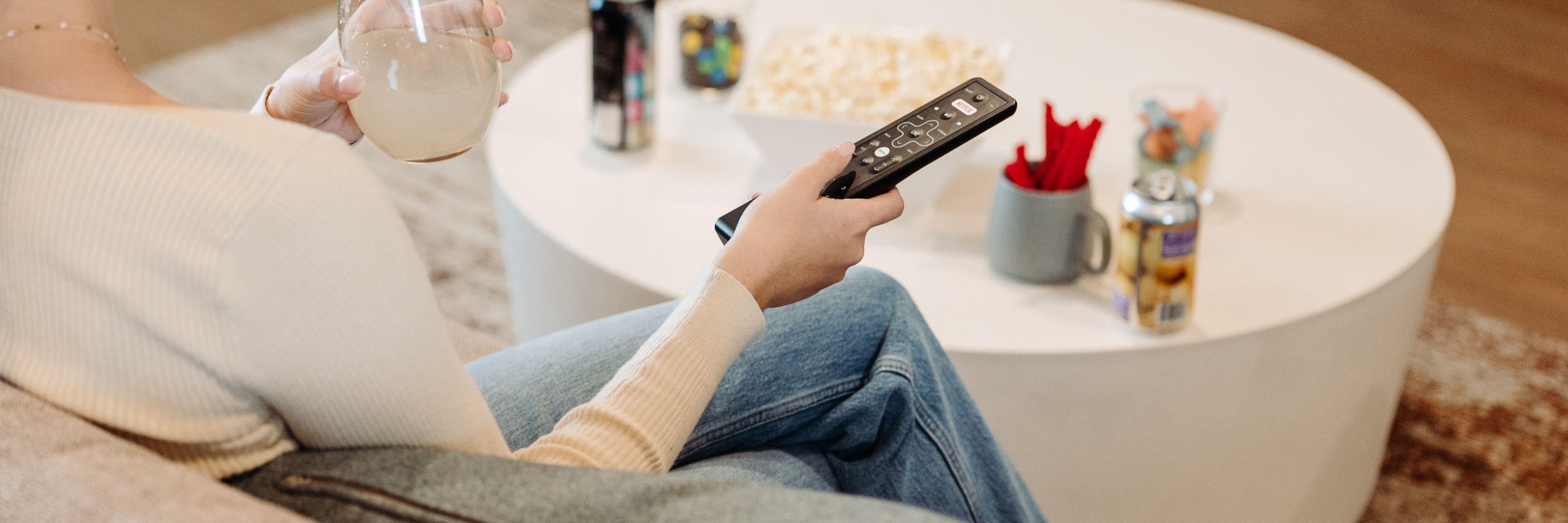 Person sitting on a couch with a drink and the television remote control